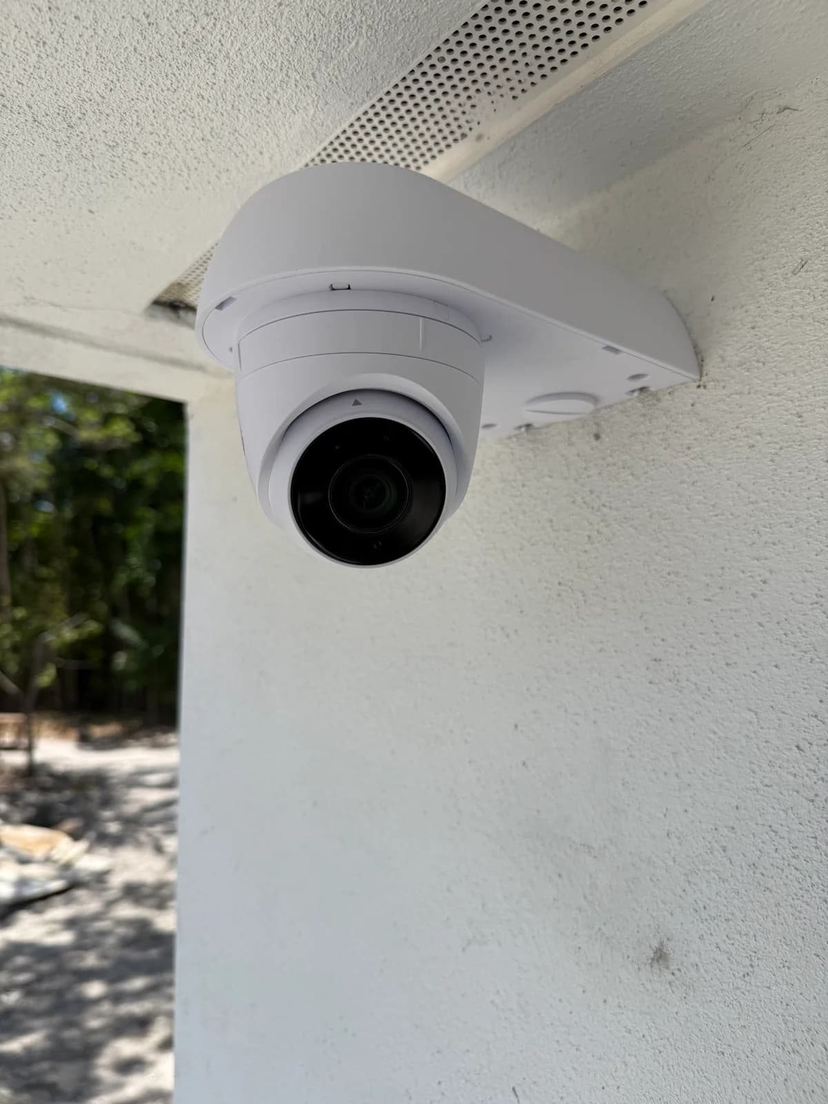 Ubiquiti dome camera mounted on stucco wall next to louvered attic vent